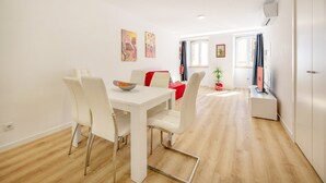 Un comedor moderno y bien iluminado con una mesa y sillas blancas, un sofá rojo y obras de arte en las paredes.
