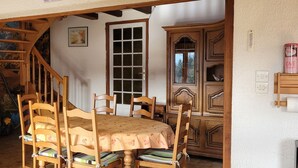 Un espace repas avec une table et des chaises en bois, un escalier et une vue sur l’extérieur.