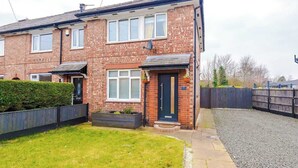 A two-story brick house with a front door, windows, and a small front garden. - Driveway | Modern Home In Altrincham | Sleeps 7 (Altrincham)