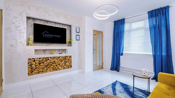 A modern living room with a fireplace, a flat-screen TV, a sofa, and a window with curtains. - Driveway | Modern Home In Altrincham | Sleeps 7 (Altrincham)