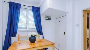 A room with a wooden table, blue curtains, a radiator, a door, and a small electronic device on the wall. - Driveway | Modern Home In Altrincham | Sleeps 7 (Altrincham)