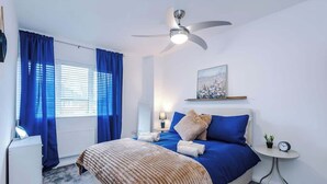 A bedroom with a bed, a ceiling fan, a bedside table with a lamp, and a window with curtains. - Driveway | Modern Home In Altrincham | Sleeps 7 (Altrincham)