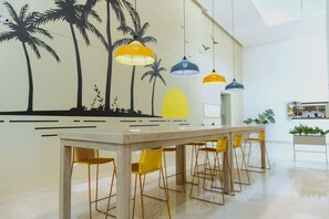 Uma cozinha moderna com armários brancos, uma ilha central com banquetas e um mural na parede com palmeiras e um sol.