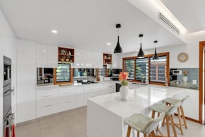 A modern kitchen with white cabinetry, a central island, pendant lighting, and a view of the outdoors.