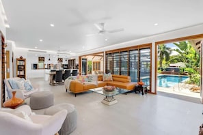 A spacious living area with a sofa, ottoman, and coffee table, a dining area with chairs and a table, and a large sliding glass door leading to a pool.