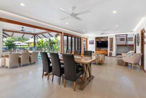 A spacious dining area with a large table and chairs, a ceiling fan, and a view of the outdoors.