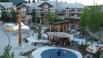 Un parque infantil con una zona circular azul, rodeado por una plaza con bancos y árboles.