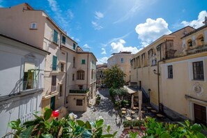 A narrow street with buildings on either side, a small courtyard with outdoor seating, and a clear blue sky.