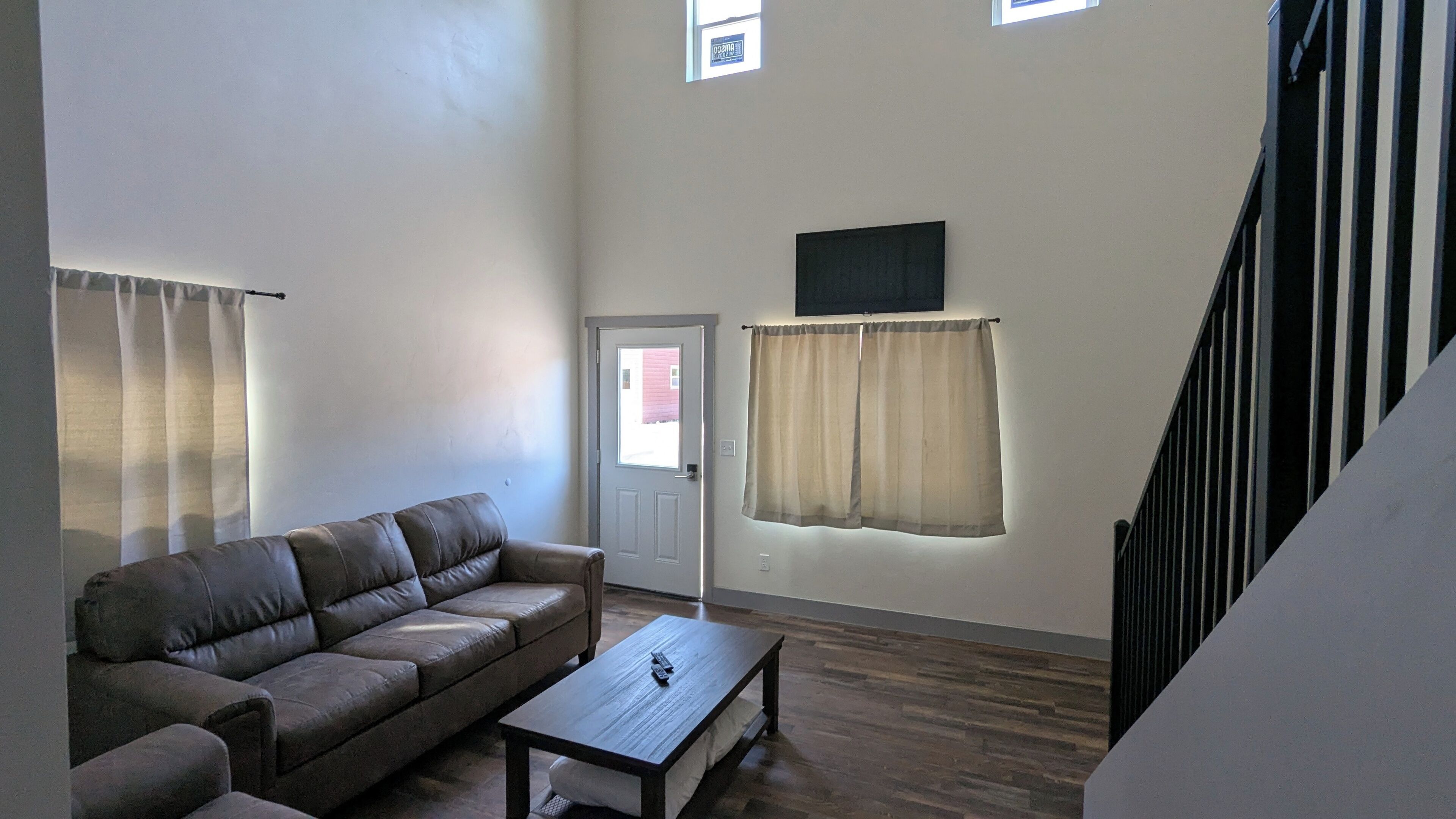 A spacious living room with a brown leather sofa, a wooden coffee table, and a door leading to a red building.