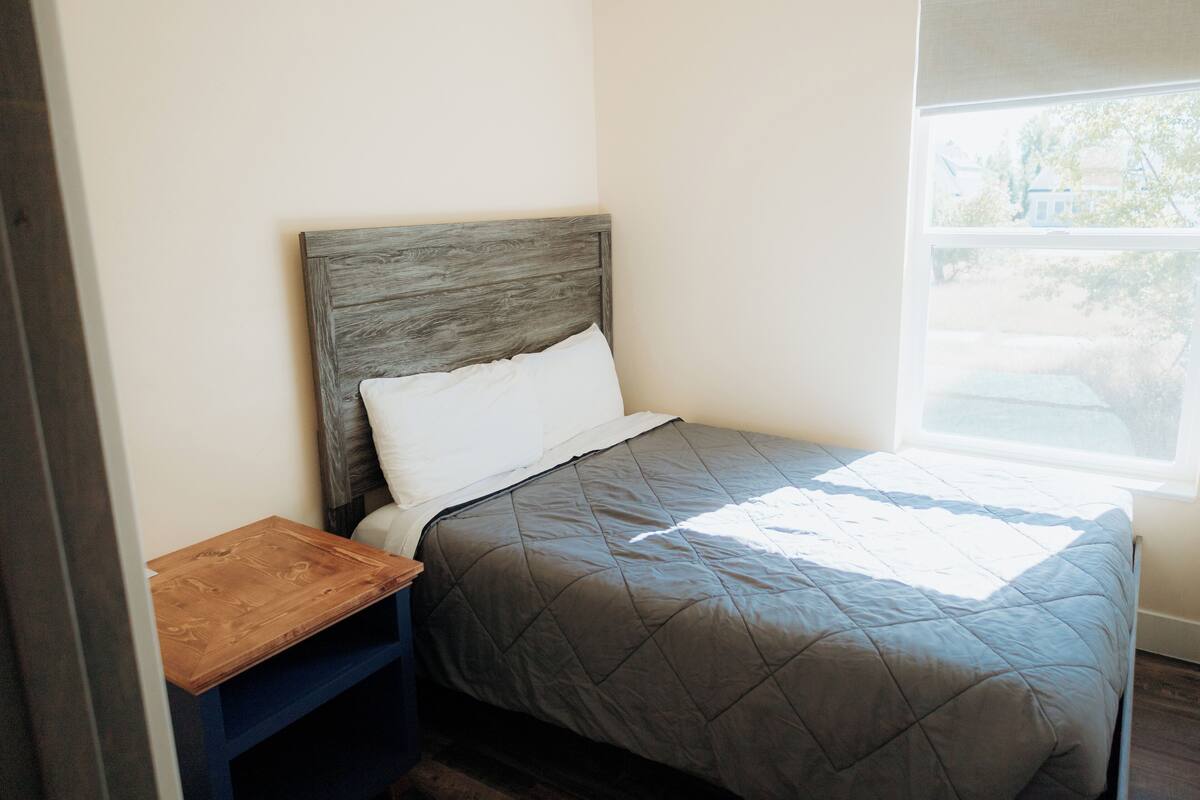 Una cama individual con cabecera de madera y colcha gris acolchada.