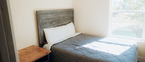 A single bed with a wooden headboard and a quilted grey bedspread.