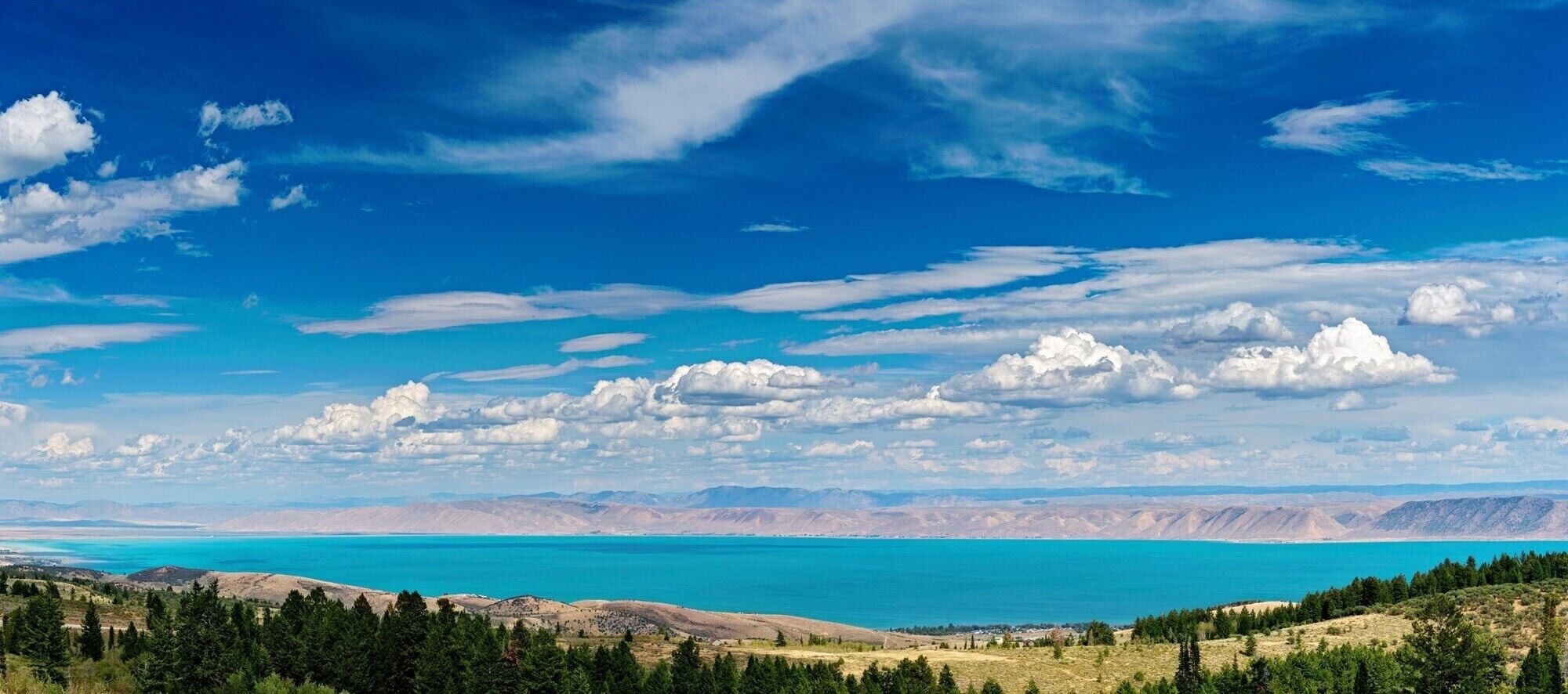Vista panorâmica de um lago rodeado por montanhas e um céu claro.