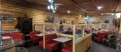 Un restaurante acogedor con paredes de madera, asientos tipo cabina rojos y un ventilador de techo.