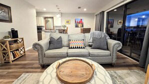 Ein modernes Wohnzimmer mit grauem Sofa, gemusterten Kissen, einer Holztablett und einem sechseckigen Teppich.