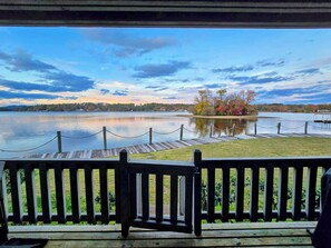 Une terrasse en bois offrant une vue sur un lac, un quai et des arbres aux couleurs automnales.