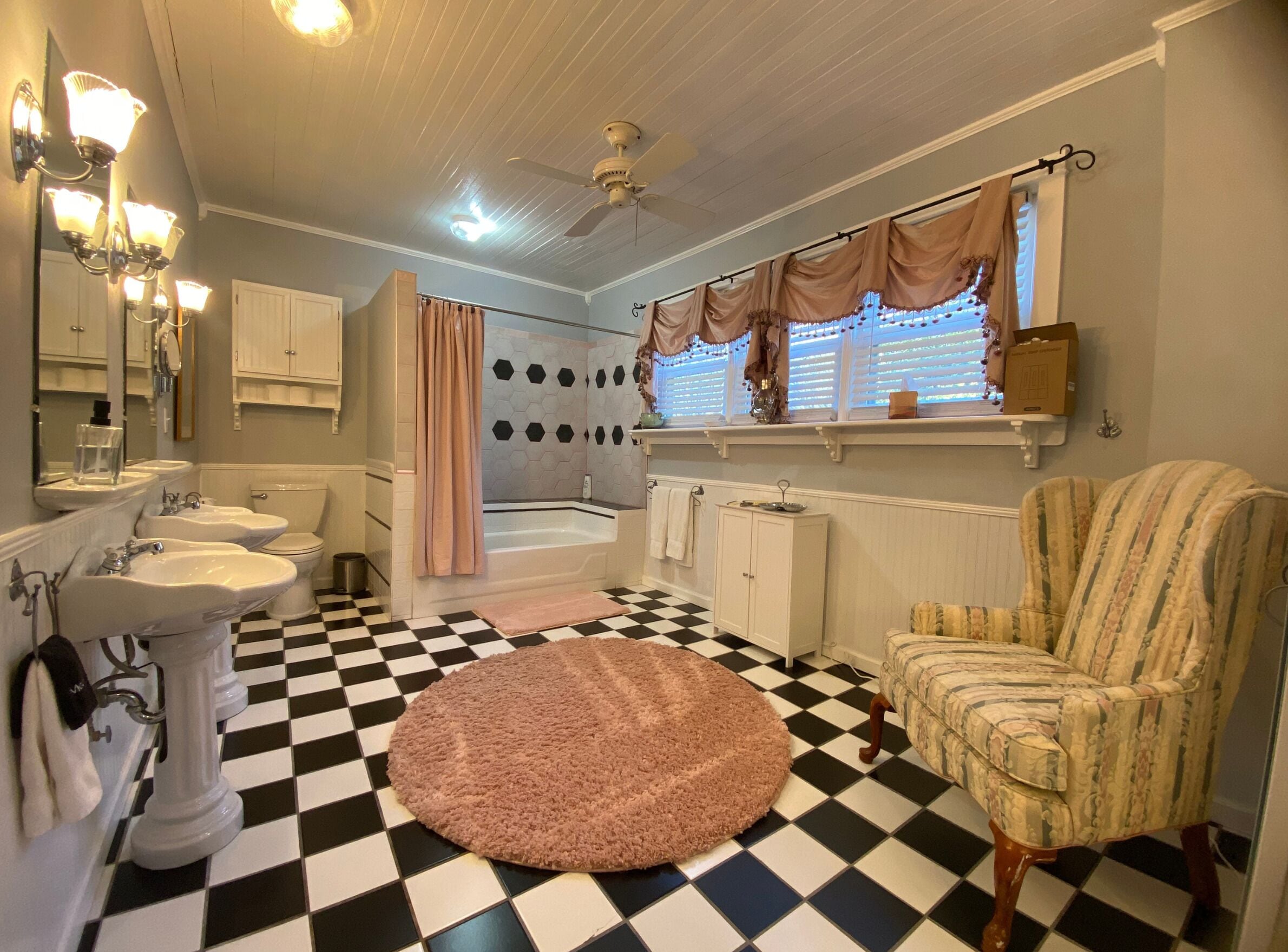 A bathroom with a checkered floor, a bathtub, a shower, and a vanity with two sinks.