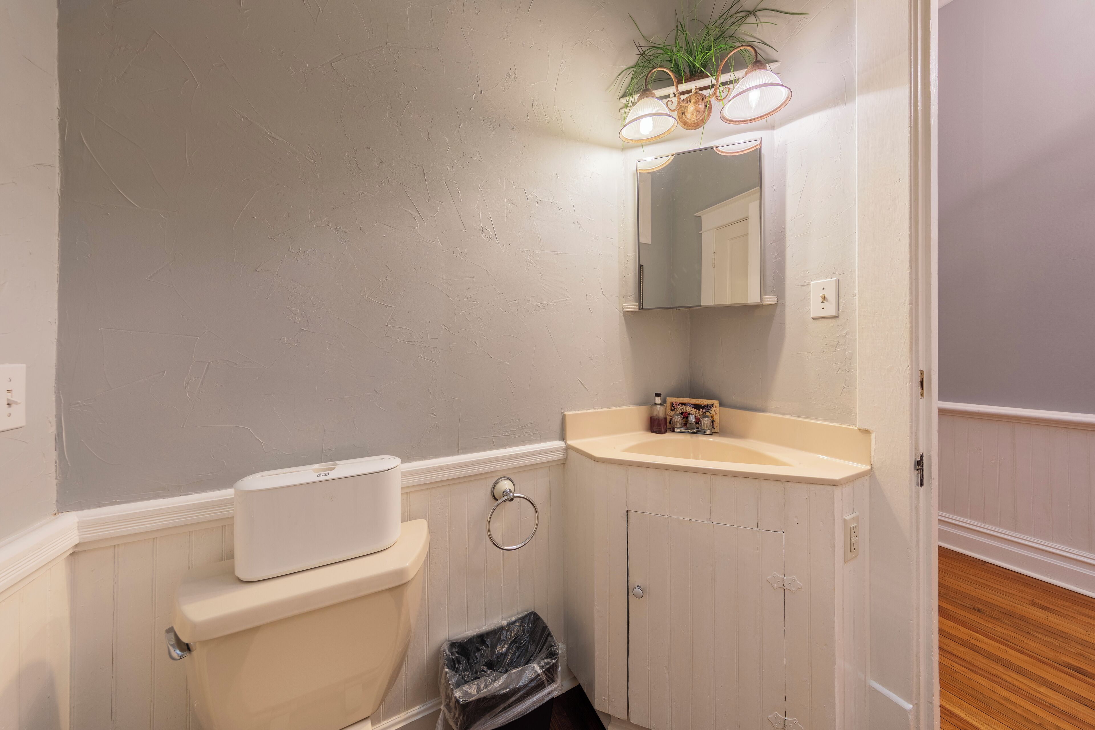 A bathroom with a toilet, sink, mirror, and a trash bin.
