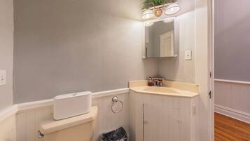 A bathroom with a toilet, sink, mirror, and a trash bin.