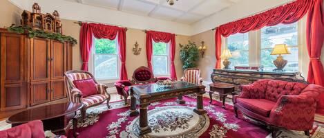 A room with a wooden cabinet, a glass-top table, red upholstered chairs, and a red carpet with floral patterns.