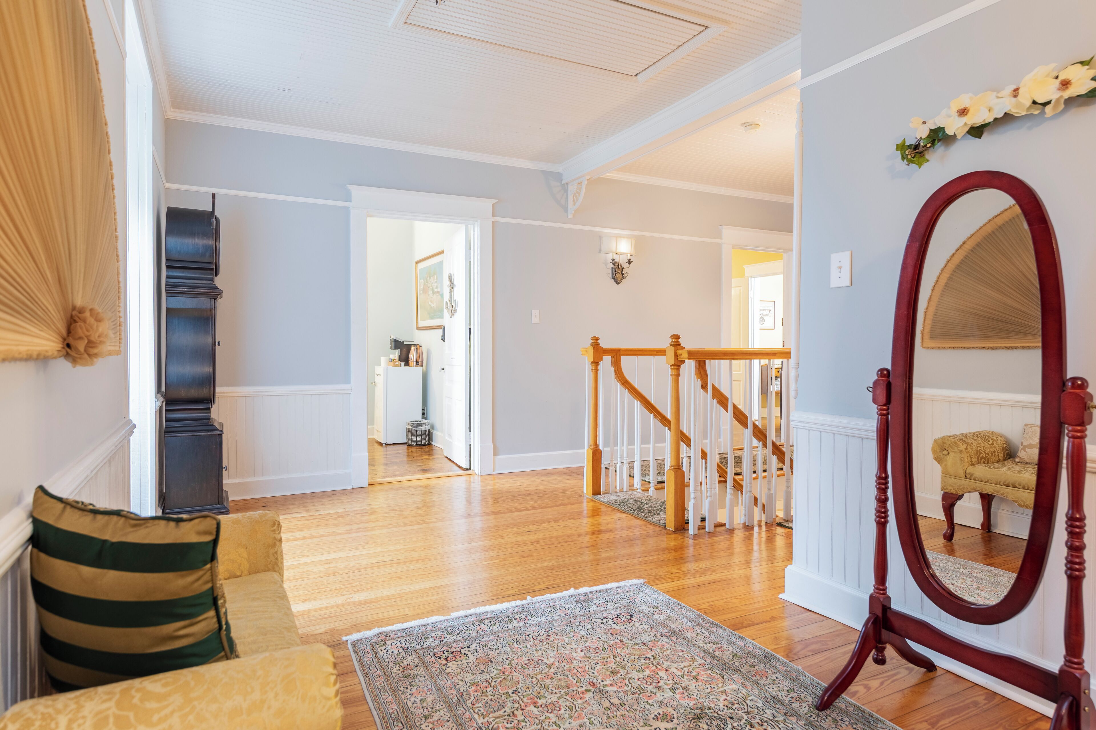 A spacious living room with hardwood floors, a large mirror, and a staircase leading to another level.