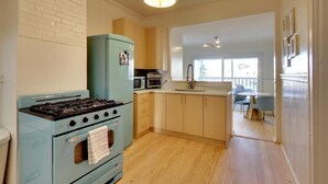 Una cocina con estufa azul, microondas y pileta. Hay una zona de comedor con mesa y sillas.
