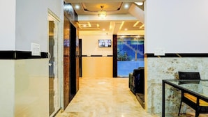 A hotel lobby with a marble floor, a reception desk, a television, and a seating area with a glass table. - Qubenest Splendour (Bangalore)