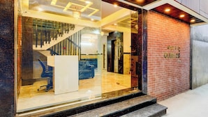 A hotel entrance with a glass facade, a staircase leading to the interior, and a brick wall with a sign. - Qubenest Splendour (Bangalore)