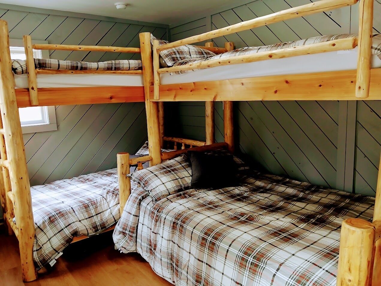 A bunk bed room with two beds, wooden walls, and a plaid bedspread.