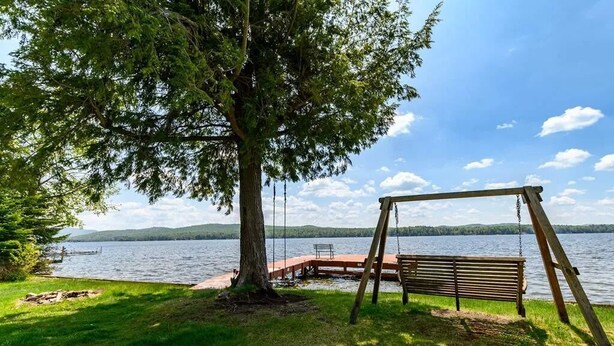 Un columpio de madera junto a un lago con un muelle que se adentra en el agua.