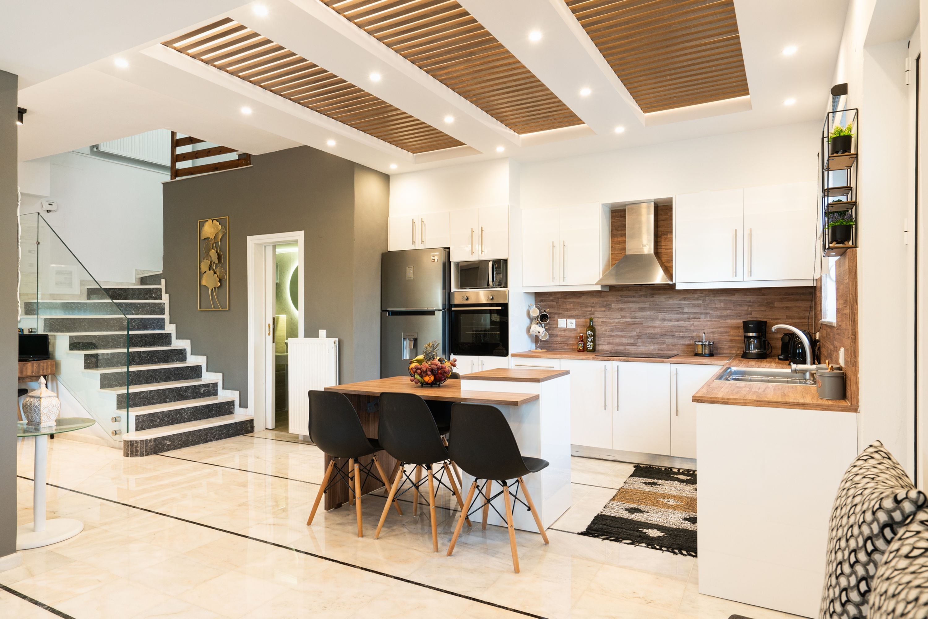 Una cocina moderna con armarios blancos, una isla de madera y un comedor con sillas negras.