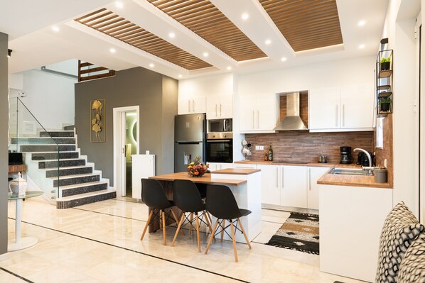 A modern kitchen with white cabinetry, a wooden island, and a dining area with black chairs.