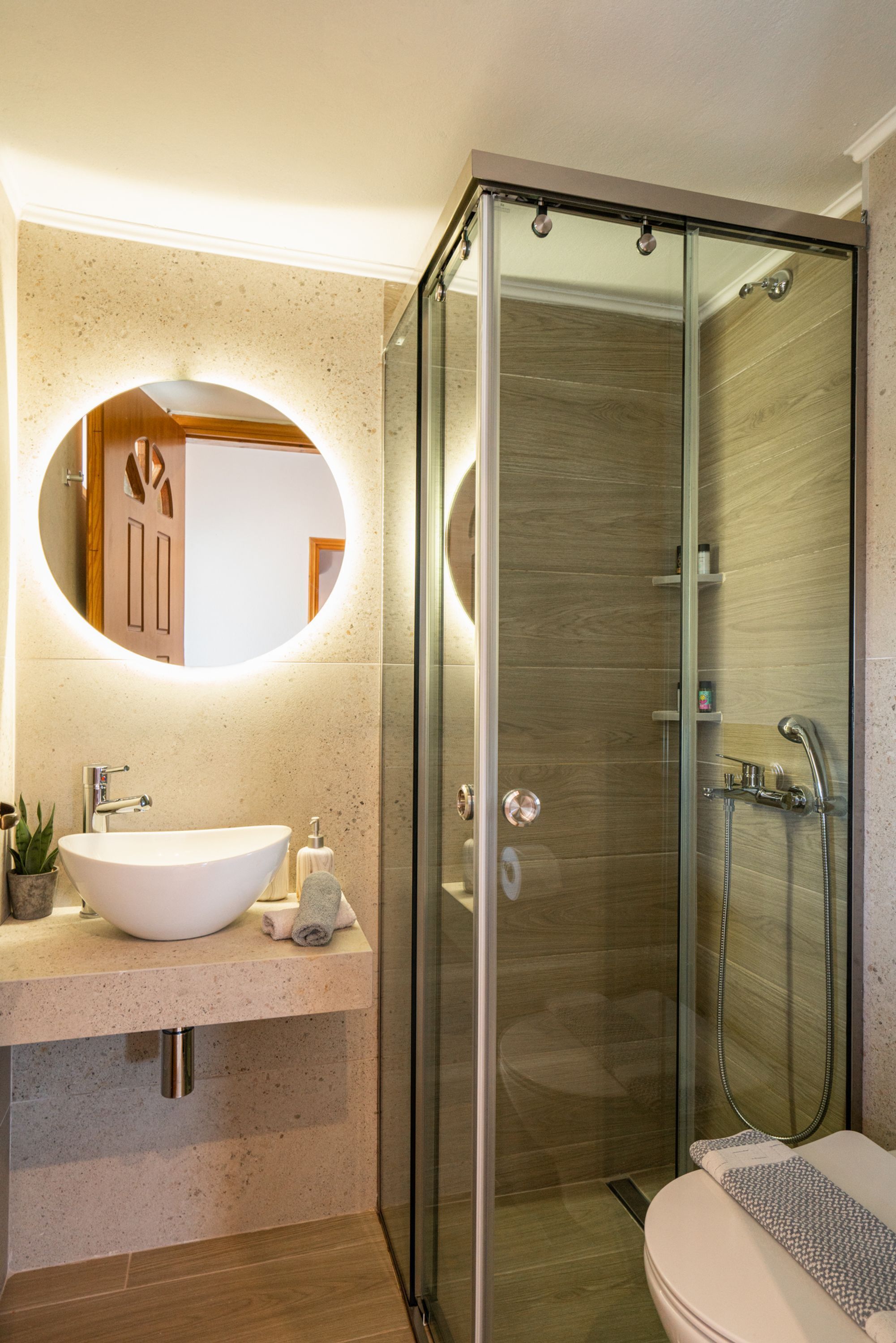 Une salle de bain moderne avec une douche en verre à porte libre, un miroir rond et un lavabo intégré.