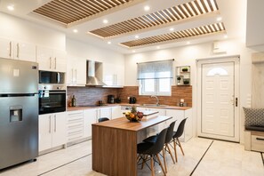 A modern kitchen with a central island, stainless steel appliances, and a wooden ceiling design.