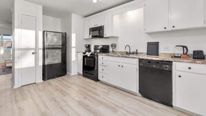 Een moderne keuken met witte kastjes, een roestvrijstalen koelkast, een magnetron, een oven, een vaatwasser en een granieten werkblad.
