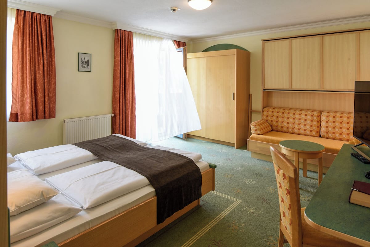 A hotel room with a bed, a sofa, a table, and a wardrobe.
