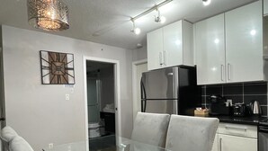 Una cocina moderna con armarios blancos, un refrigerador de acero inoxidable y una mesa de comedor de vidrio con sillas.
