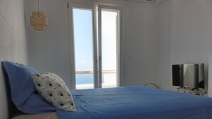A bedroom with a bed, a TV, a bedside table, and a view of the sea through a sliding door. - VILLA THEROS, 6 persons, swimming pool. Exceptional view! (NAXOS)