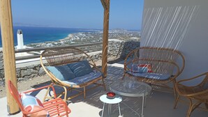 A terrace with wicker chairs and a small table, overlooking a coastal landscape with a lighthouse. - VILLA THEROS, 6 persons, swimming pool. Exceptional view! (NAXOS)