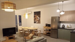 A modern living room with a flat-screen TV, a sofa, a dining table with chairs, and a kitchen area with a refrigerator, microwave, and sink. - VILLA THEROS, 6 persons, swimming pool. Exceptional view! (NAXOS)