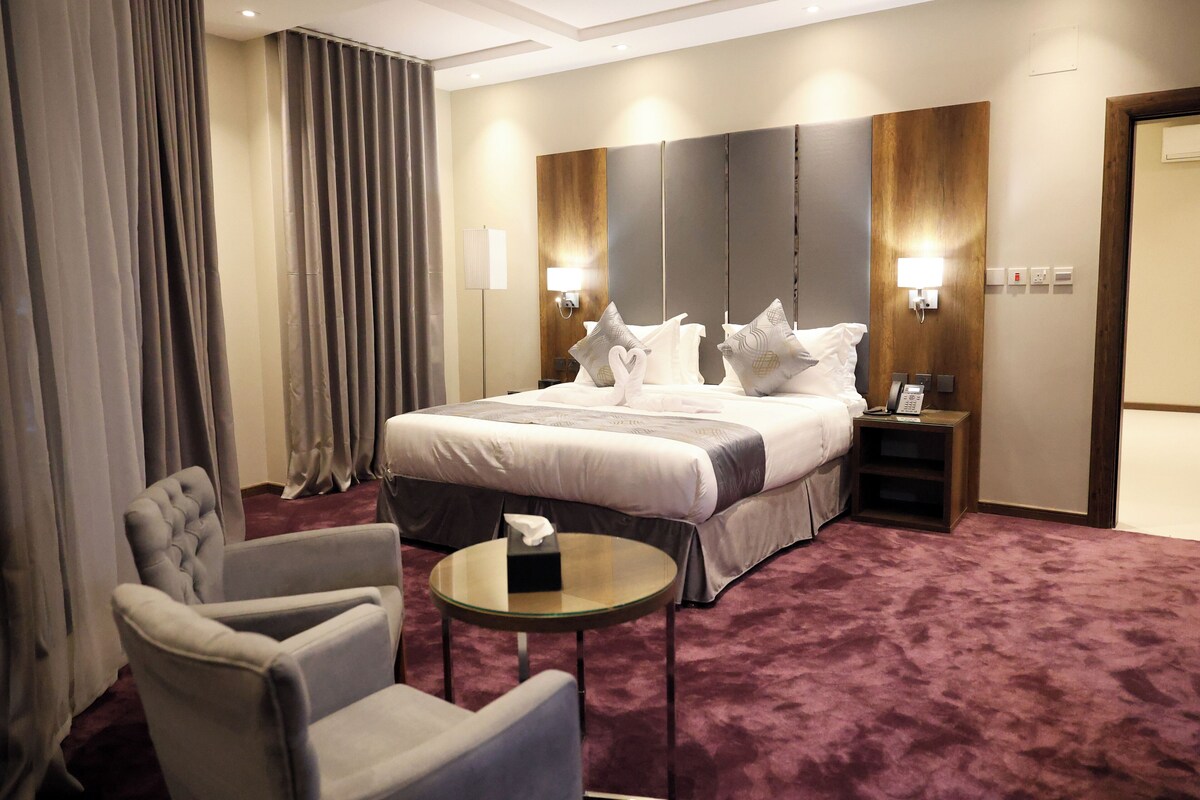 Ein Hotelzimmer mit einem großen Bett, zwei Nachttischen, einem Sessel und einem kleinen runden Tisch.