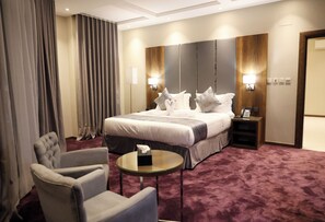 Ein Hotelzimmer mit einem großen Bett, zwei Nachttischen, einem Sessel und einem kleinen runden Tisch.