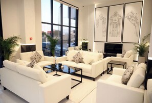 Ein modernes Wohnzimmer mit weißen Sofas, einem Glastisch und großen Fenstern mit Blick auf die Straße.