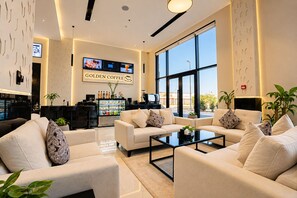 A modern lounge area with sofas, a coffee station, and large windows. - Golden Season Hotel - AR Rass (Ar Rass)