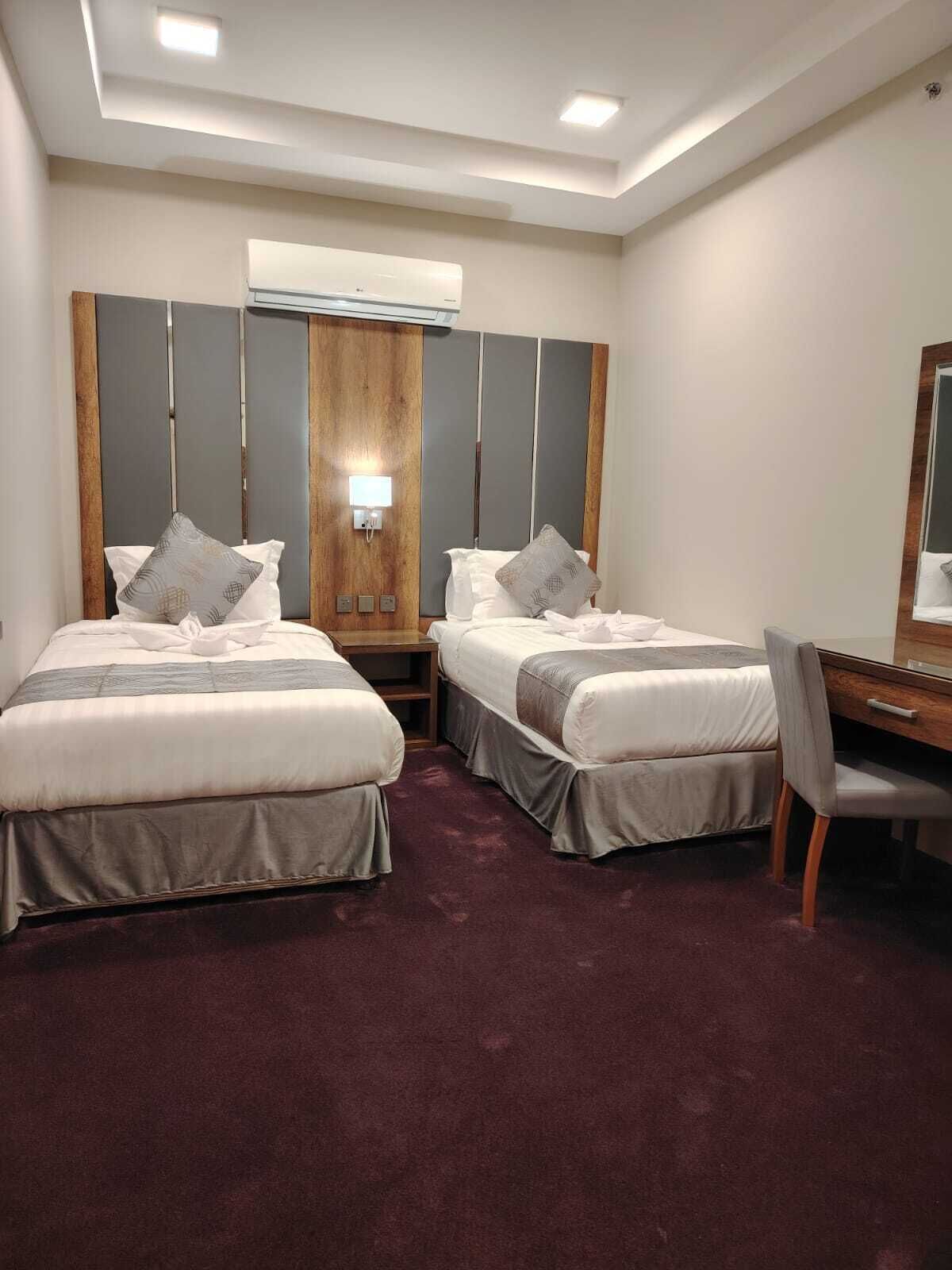 Habitación de hotel con dos camas, un escritorio y un espejo grande.