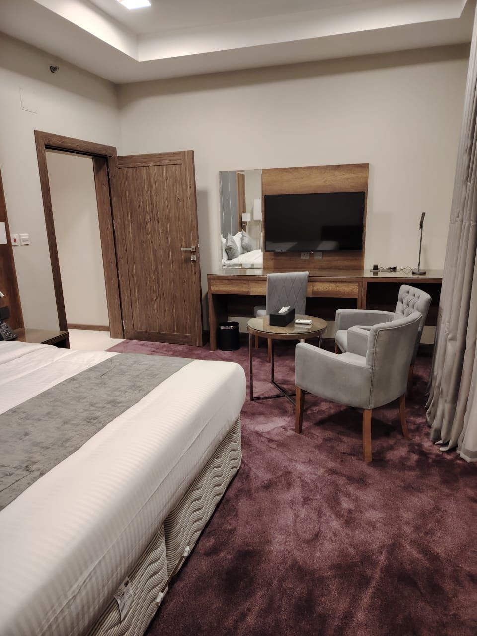 Quarto de hotel com uma cama, uma escrivaninha, uma cadeira, uma televisão e um guarda-roupa.