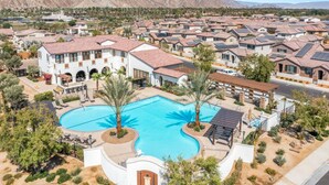A residential area with a large swimming pool surrounded by houses with red-tiled roofs and solar panels.