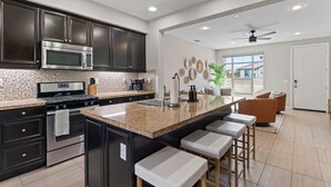 A modern kitchen with dark cabinets, a stainless steel range, and a large island with bar stools.