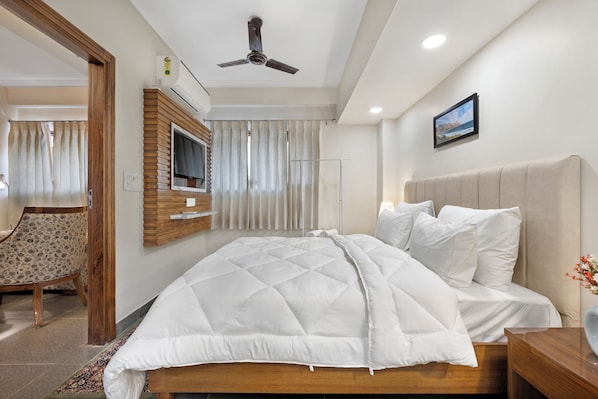 Une chambre bien rangée, avec un lit, un téléviseur fixé au mur et un ventilateur de plafond.