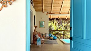 A room with a wooden ceiling, a blue door, a sofa, a chair, and a view of greenery outside. - A natural setting in Playa Grande, peaceful and relaxing place! (Playa Grande)