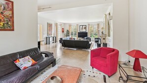 A spacious living room with a black leather sofa, a red armchair, and a marble coffee table.